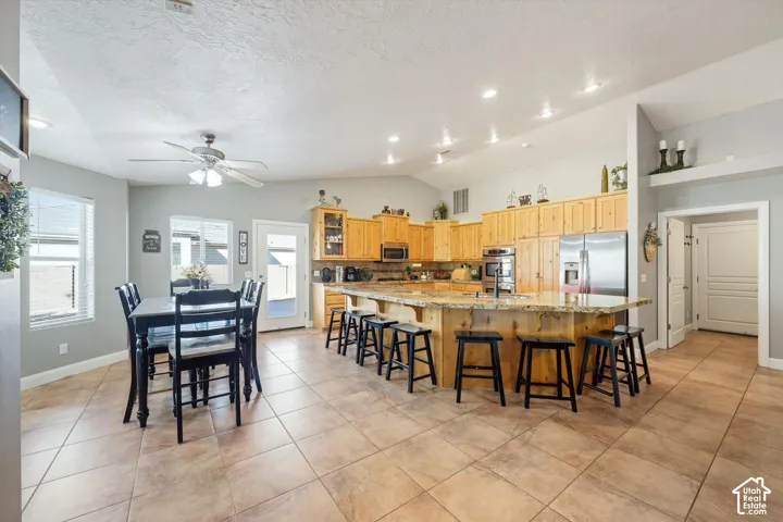 Open-concept kitchen featuring natural wood cabinetry, a large stone-topped island, tile flooring, recessed lighting, and a vaulted ceiling