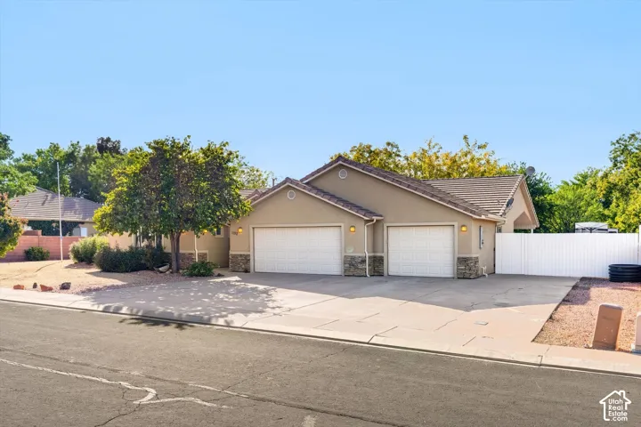 Single-story exterior featuring a stucco facade, stone veneer accents, concrete driveway, two-car garage, and white privacy fencing