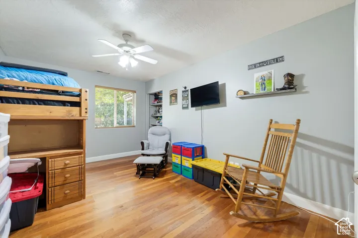 Wood-finish flooring, multi-blade ceiling fan with integrated lighting, and a single-hung window with wood-trim framing