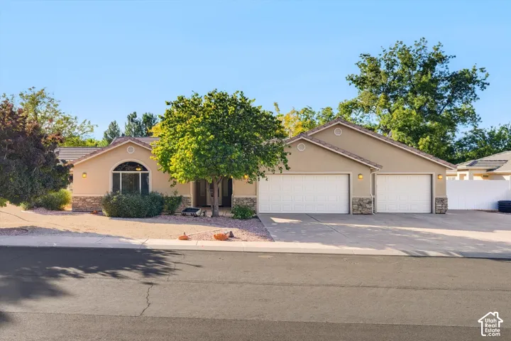 Single-level exterior featuring tan stucco siding, stone veneer accents, an arched window, and a three-car garage