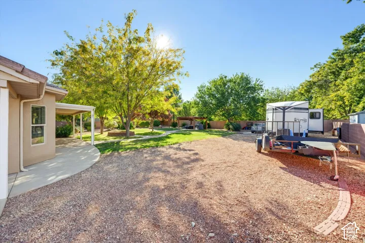 Expansive backyard featuring a covered concrete patio, mature trees, a dedicated stone-paved walkway, and perimeter masonry wall fencing