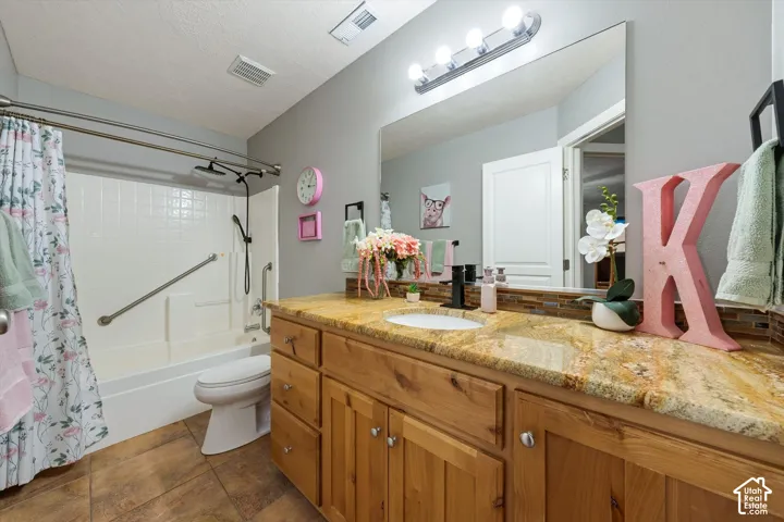 Bathroom featuring natural stone-finish countertops, warm-toned wood cabinetry, tile flooring, a large wall-mounted mirror, and a tub-shower combination with integrated safety bars