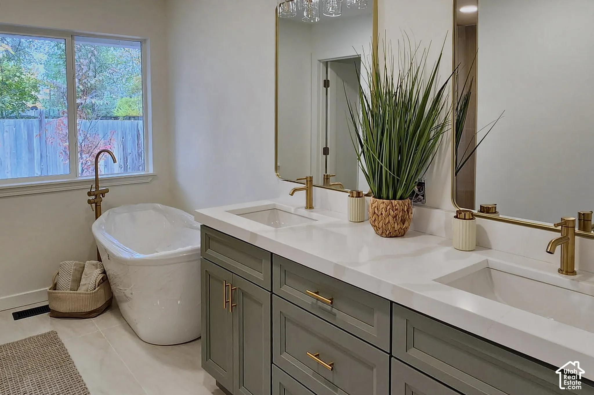 Dual-sink vanity with a quartz countertop, soft-green cabinetry, brass-toned fixtures, oval freestanding soaking tub, and arched mirrors