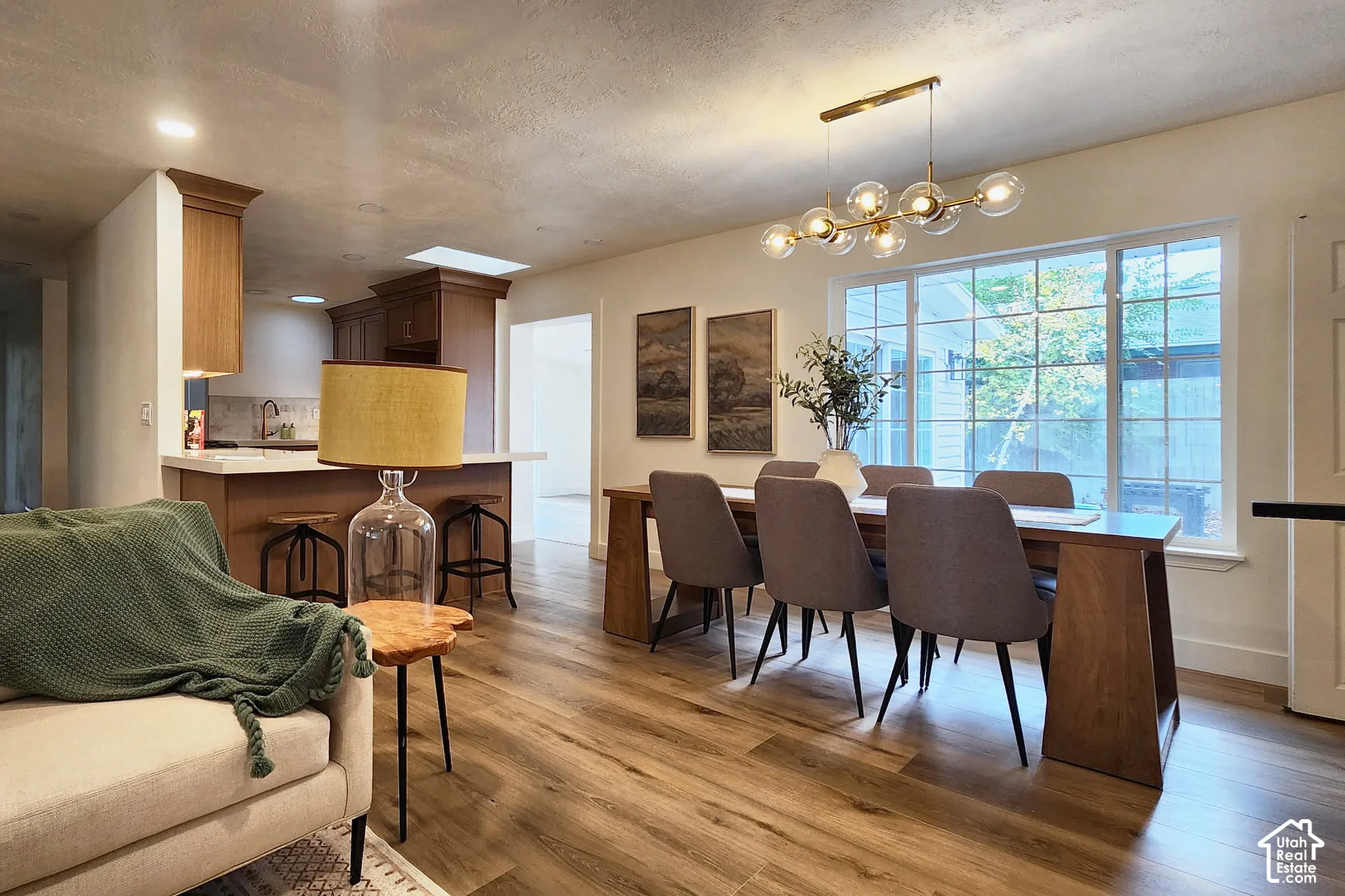 Open-concept interior featuring wood-finish flooring, a multi-light globe chandelier, large grid-pattern windows, and custom wood cabinetry with a breakfast bar