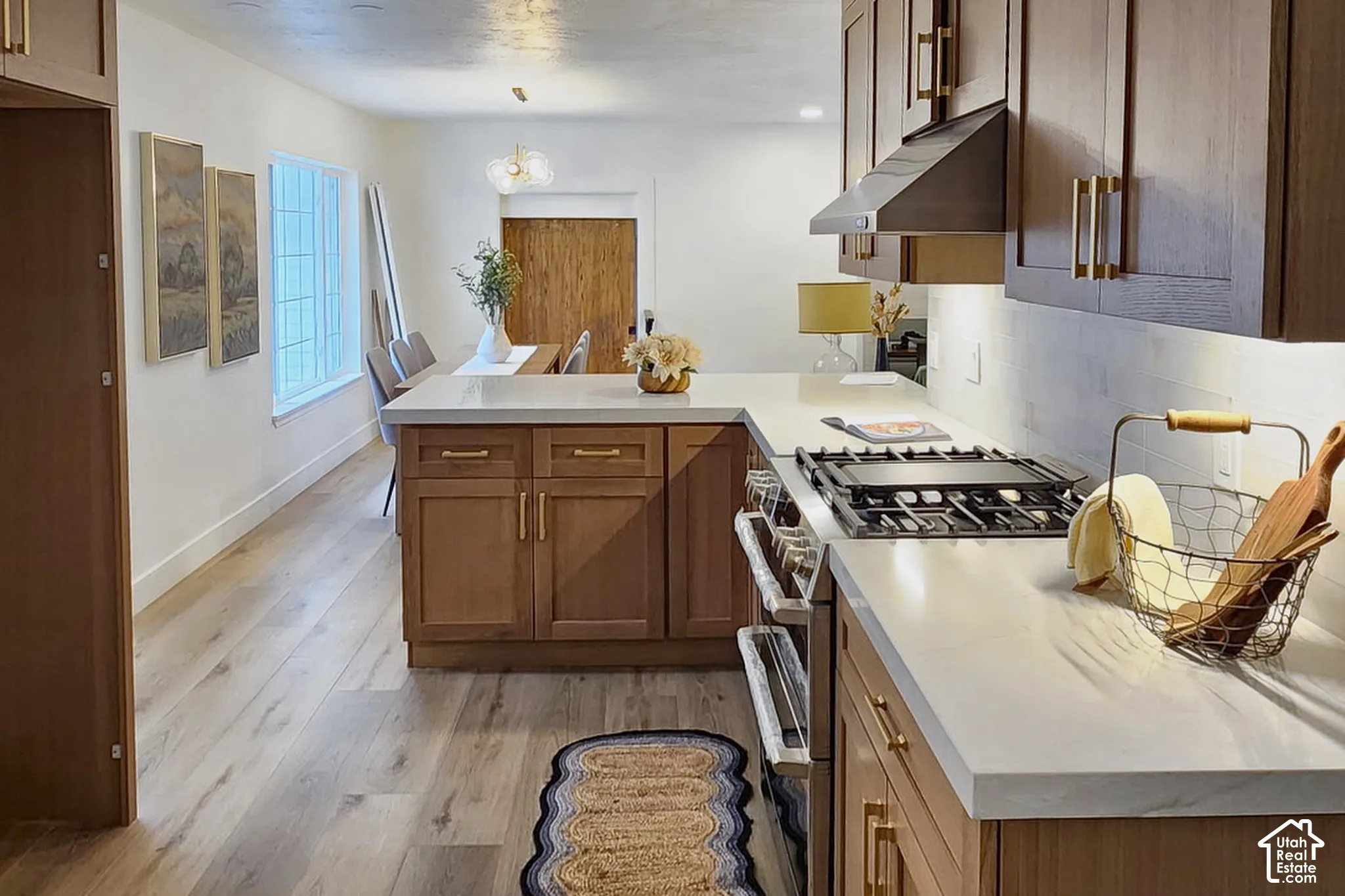 Kitchen featuring custom cabinetry with brass hardware, quartz countertops, integrated gas range, range hood, and wood-finish flooring