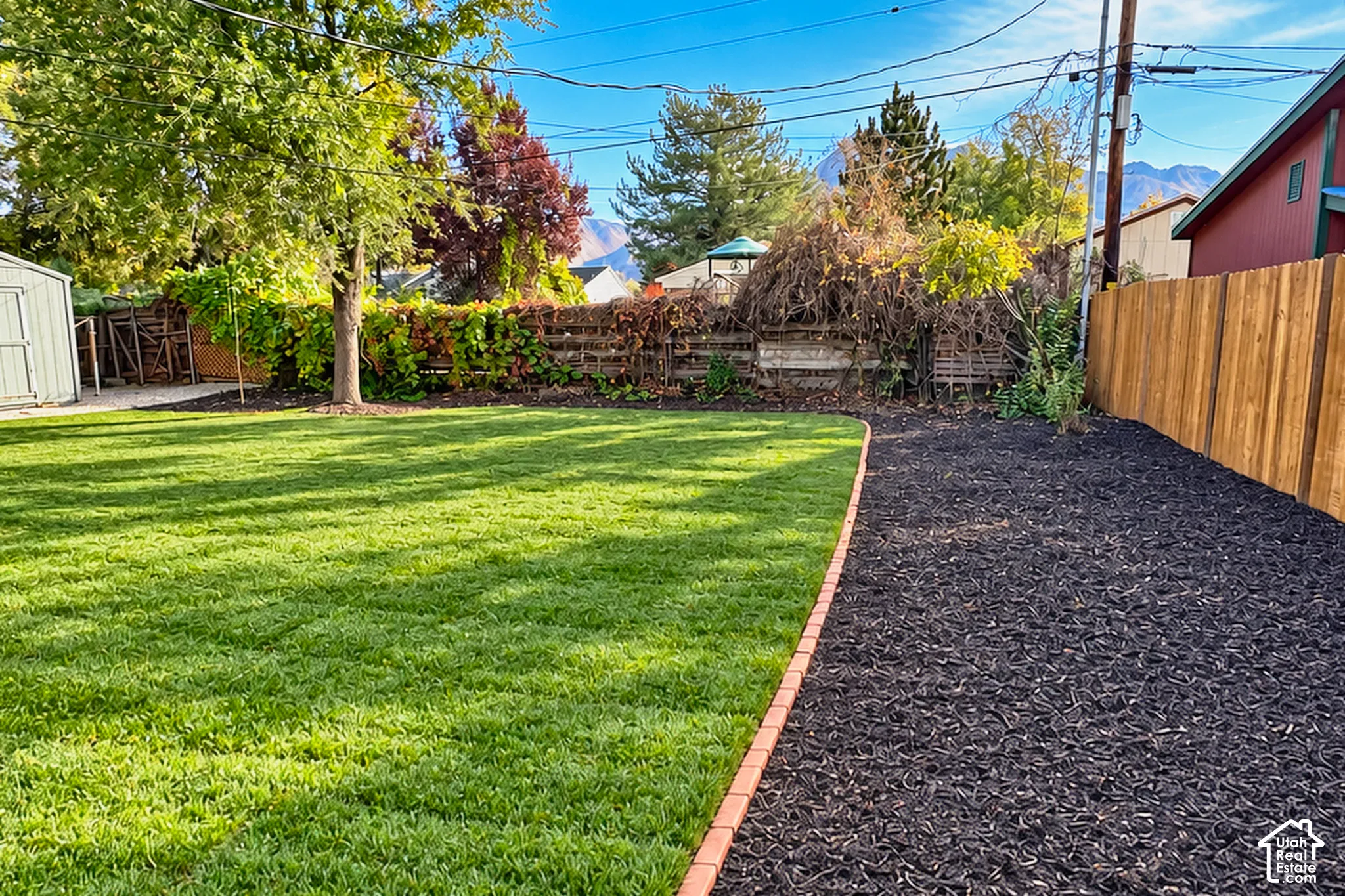 Backyard featuring a manicured lawn, brick paver edging, dark mulch ground cover, and wood privacy fencing, with mountain range backdrop