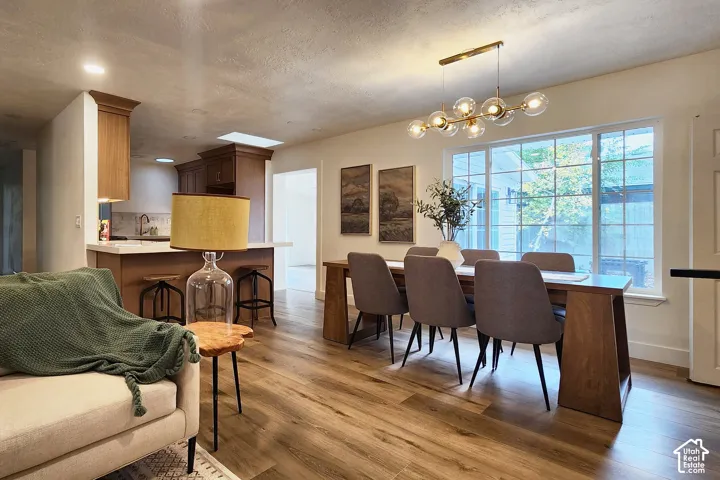 Open-concept interior featuring wood-finish flooring, a multi-light globe chandelier, large grid-pattern windows, and custom wood cabinetry with a breakfast bar