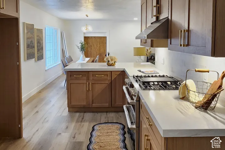 Kitchen featuring custom cabinetry with brass hardware, quartz countertops, integrated gas range, range hood, and wood-finish flooring