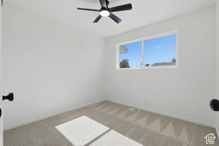 Room featuring neutral-toned carpeting, a dual-pane sliding window, and a matte black ceiling fan with integrated lighting