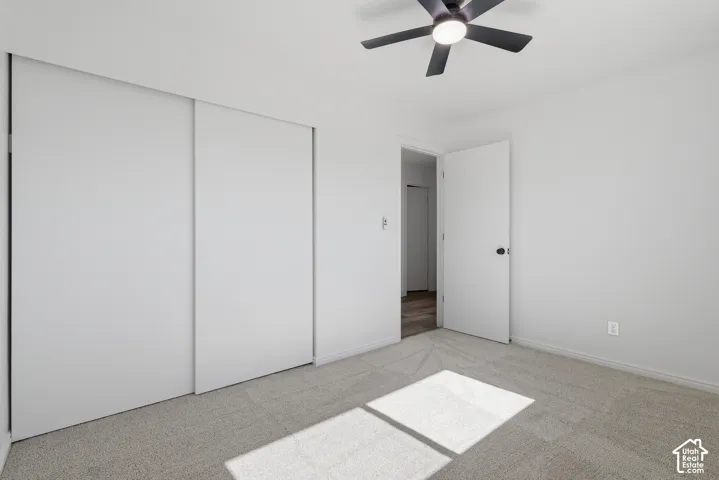 Neutral-toned carpeting, sliding closet doors, and a ceiling fan with integrated lighting