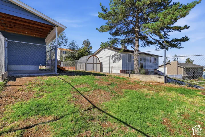 Outdoor area featuring a chain-link fenced perimeter, concrete retaining wall, detached storage structure, and mature tree
