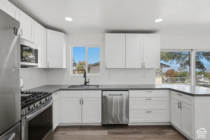 Kitchen featuring white cabinetry, solid-surface countertops, stainless steel appliances, a matte black kitchen faucet, and wood-finish flooring