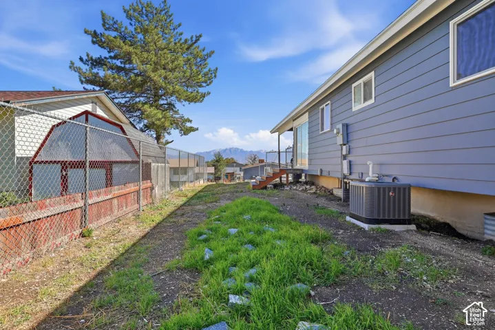 Exterior featuring horizontal siding, chain-link perimeter fencing, and an outdoor HVAC unit, set against a mountain backdrop