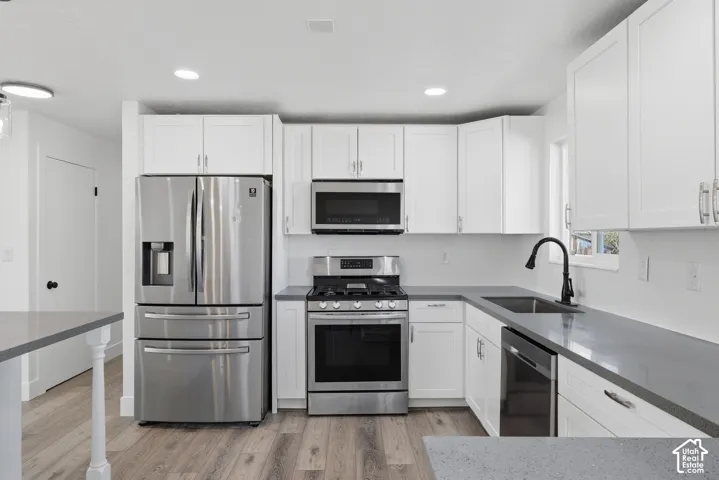 Kitchen featuring white shaker-style cabinetry, stainless steel appliances, dark stone-finish countertops, wood-finish flooring, and a matte black gooseneck faucet