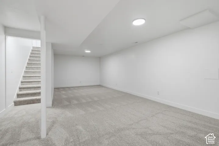 Finished lower-level room featuring neutral wall-to-wall carpeting, recessed ceiling lighting, and a structural support column