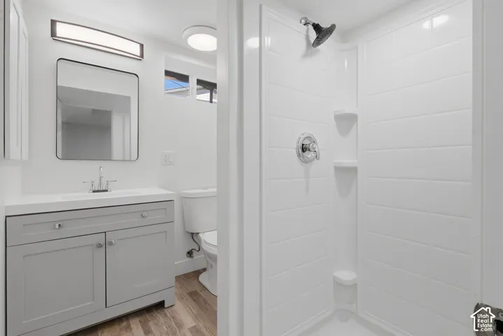 Bathroom featuring a grey vanity with a white countertop, rectangular mirror with thin frame, wall-mounted light fixture, and a white tile-surround shower