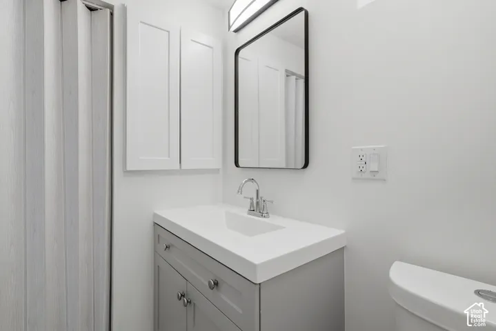 Bathroom featuring a vanity with a white countertop and integrated sink, a rectangular mirror with a black frame, wall-mounted light fixture, white Shaker-style cabinetry, and a folding door