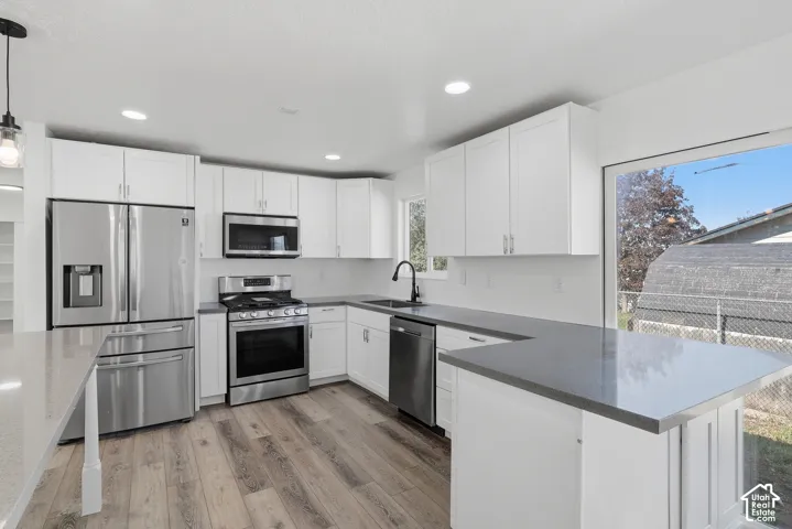 Kitchen featuring white shaker cabinetry, stainless steel appliances, dark solid-surface countertops, recessed lighting, and wood-finish flooring