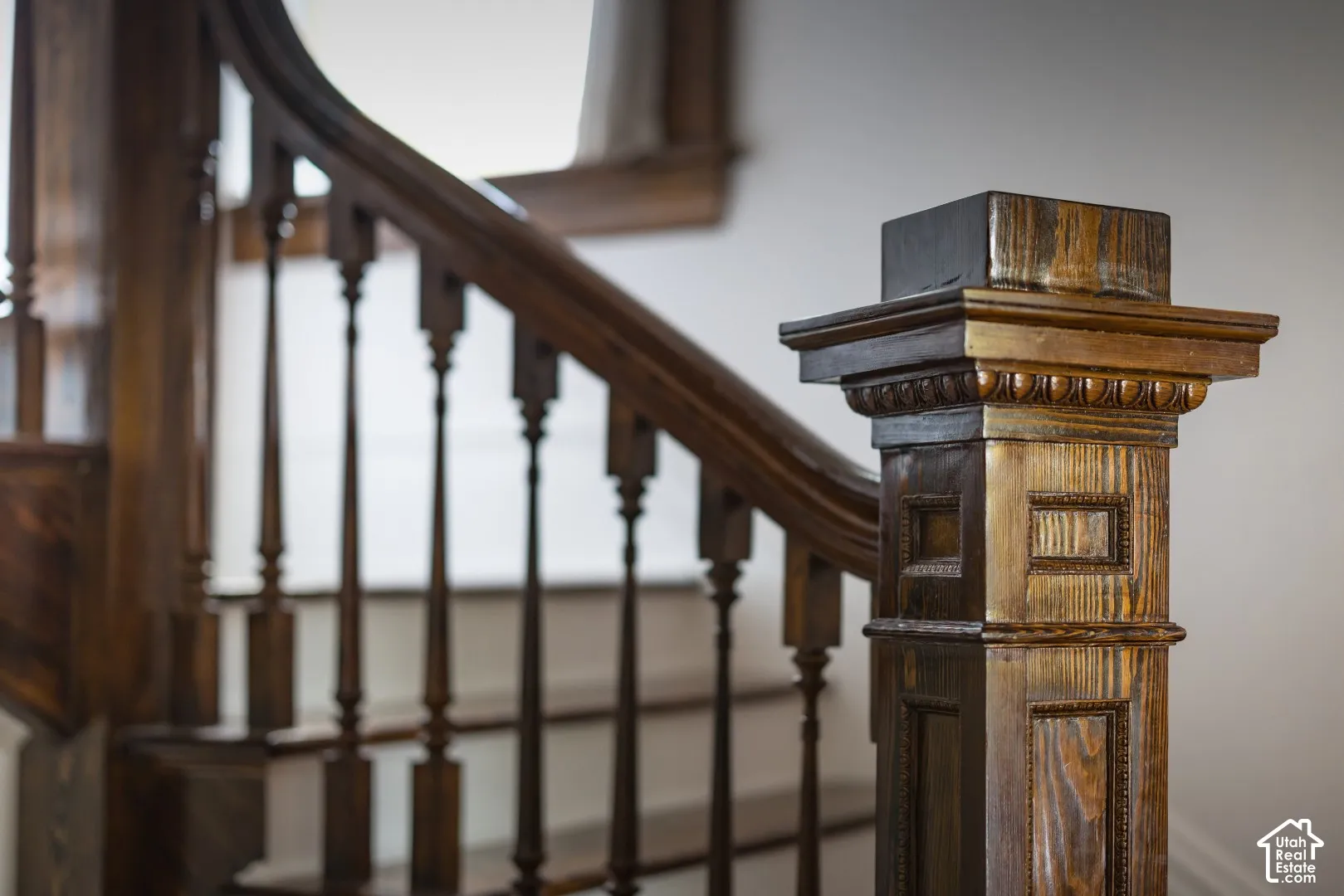 Staircase featuring a rich-toned wood newel post with carved detailing, turned balusters, a curved handrail, and wood-finish treads