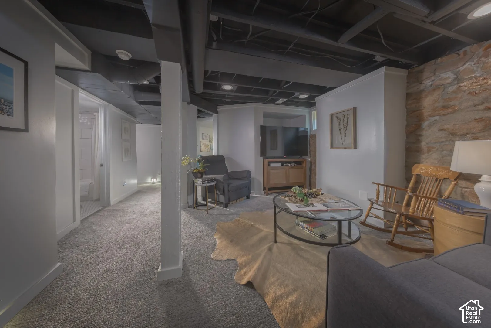 Finished interior space featuring an exposed stone feature wall, neutral carpeting, recessed ceiling lighting, and an industrial-style painted open-joist ceiling