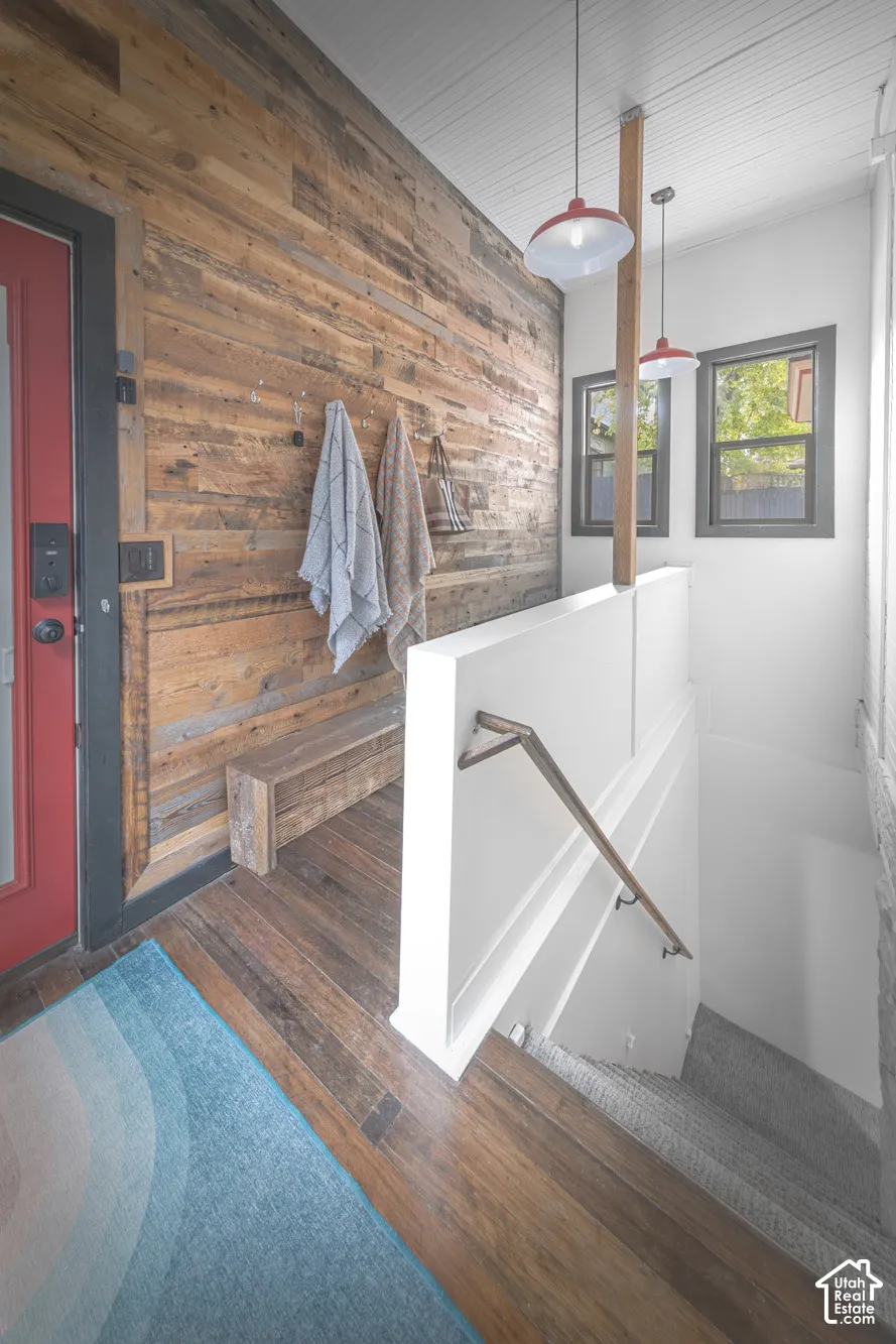 Entryway featuring a reclaimed wood accent wall, wood-finish flooring, metal handrail, beadboard ceiling, and dual pendant light fixtures