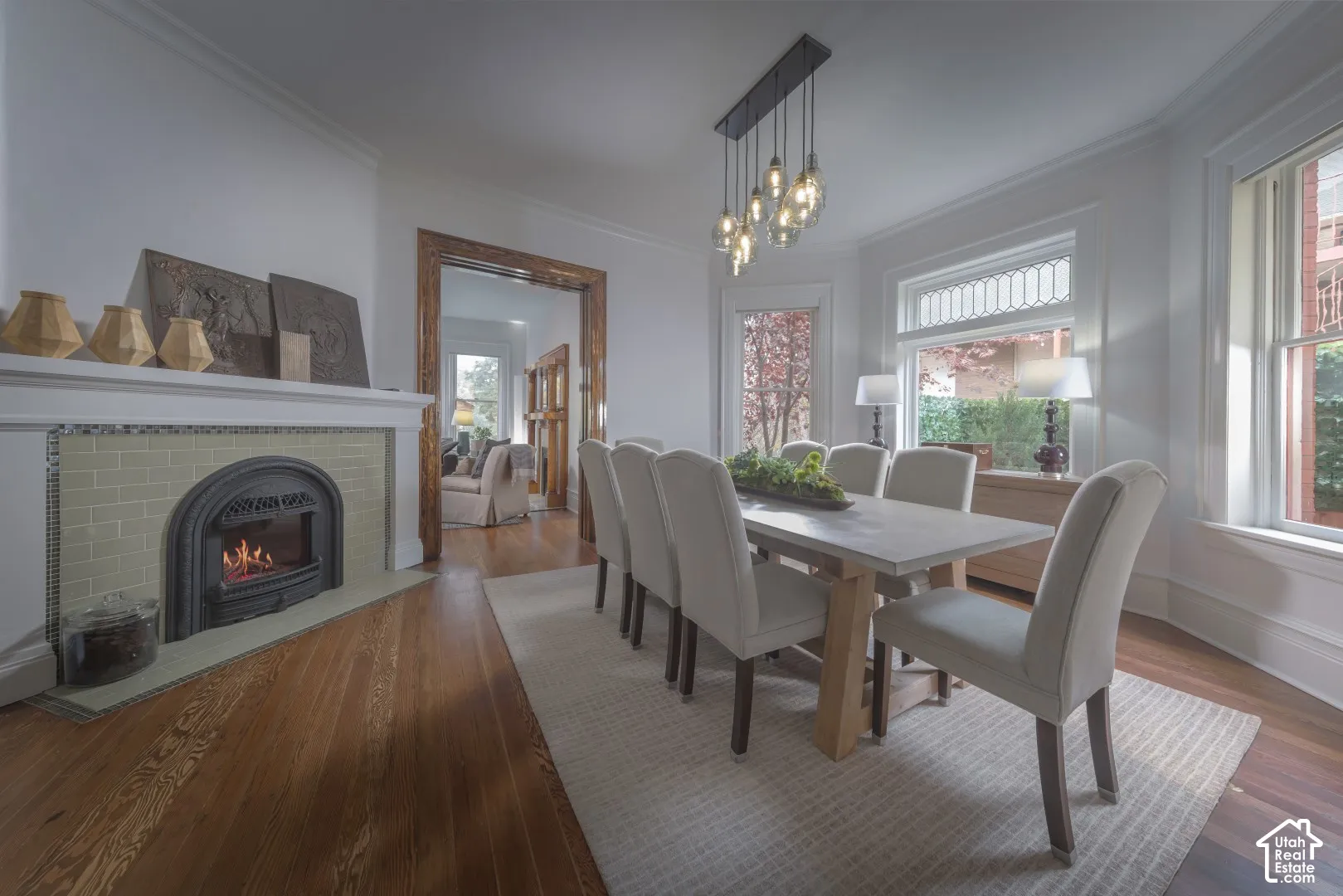 Fireplace with green tile surround and mantle, multi-pane transom windows, wood-finish flooring, and multi-bulb pendant lighting
