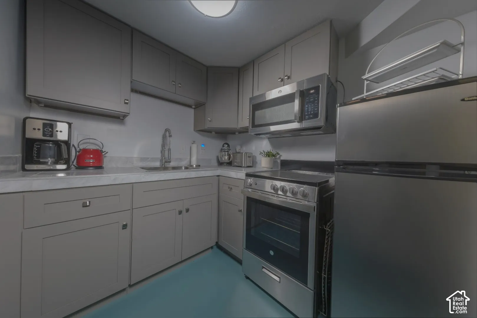 Kitchen featuring grey shaker-style cabinetry, solid-surface countertops, and a full suite of stainless steel appliances including an over-the-range microwave and electric range