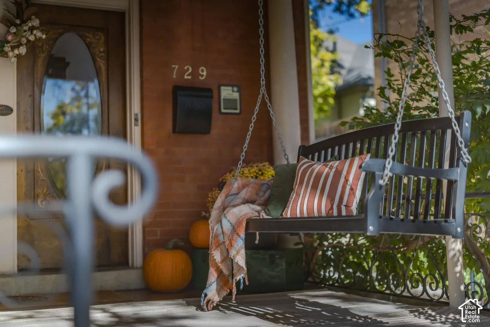 Covered front porch featuring brick masonry, a wood entry door with an oval glass insert, and a chain-suspended porch bench