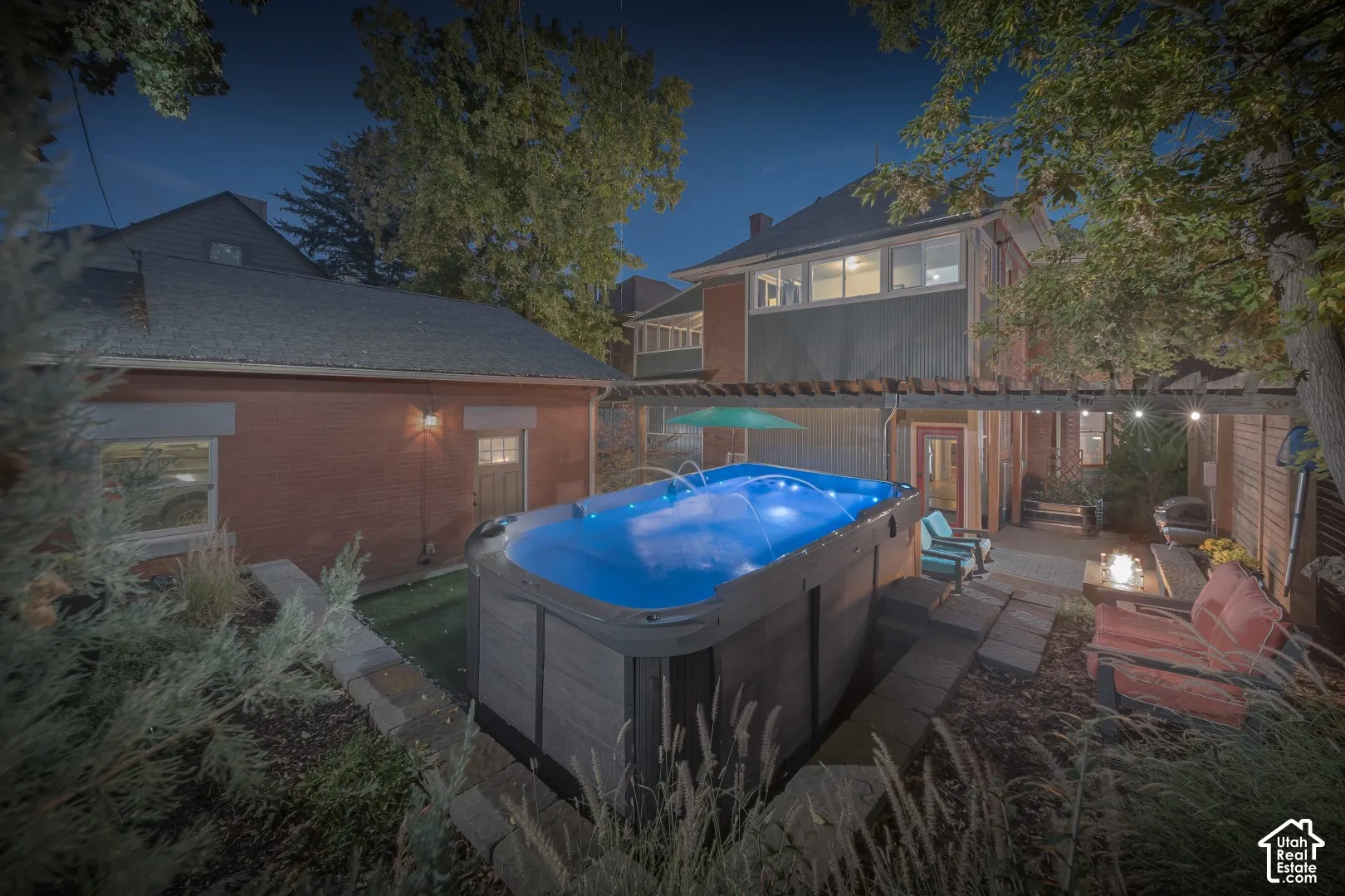 Backyard exterior featuring an above-ground swim spa, a wooden pergola, brick siding, and stone hardscaping
