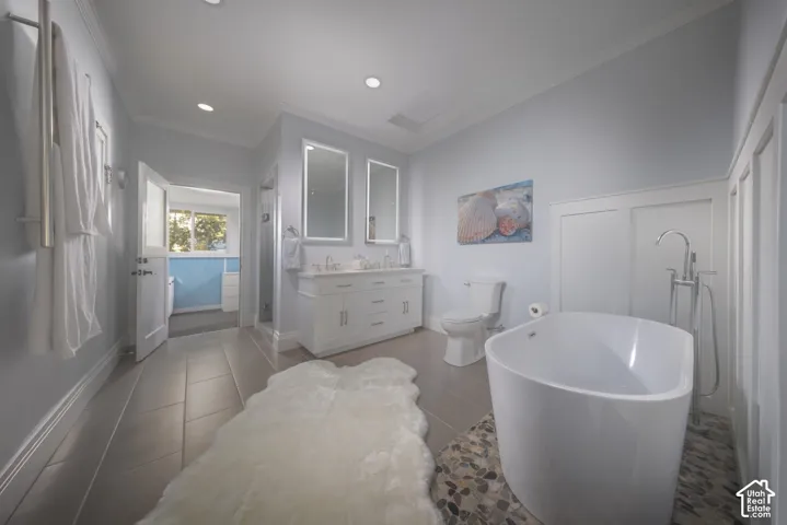 Freestanding soaking tub with floor-mounted chrome faucet, stone-tiled floor inlay, dual-vanity with integrated lighting, and white wainscoting