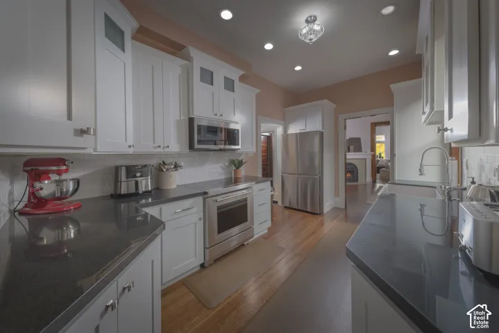 Kitchen featuring white shaker-style cabinetry, dark stone countertops, subway tile backsplash, stainless steel appliances, and wood-finish flooring