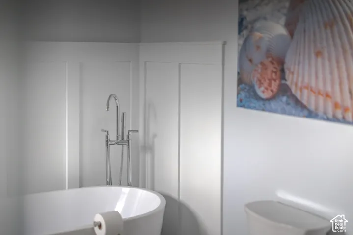 Freestanding soaking tub featuring a chrome floor-mounted faucet with a handheld sprayer, accented by white wainscoting wall paneling