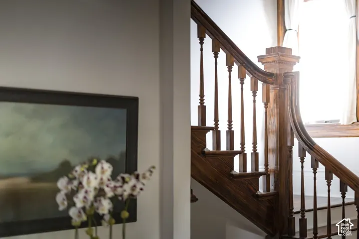 Staircase featuring a rich-toned wood handrail, matching decorative balusters, and a substantial, carved newel post
