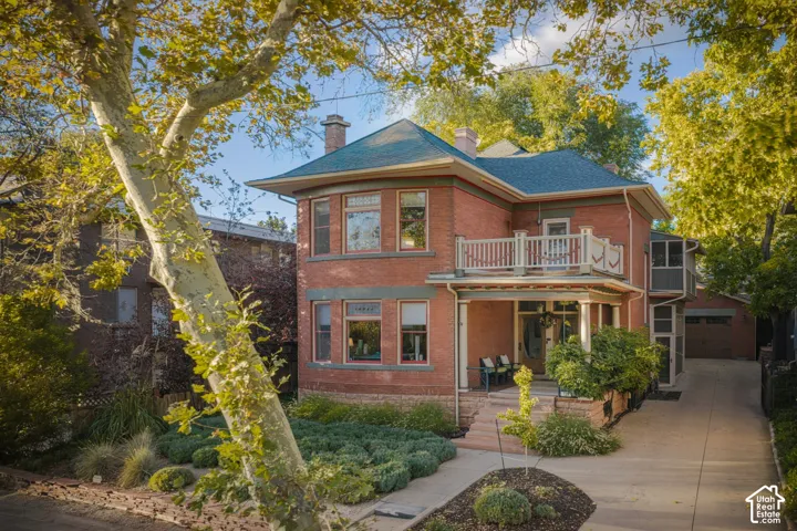 Two-story brick exterior featuring a covered front porch, an upper-level balcony with white balustrades, and a paved side driveway
