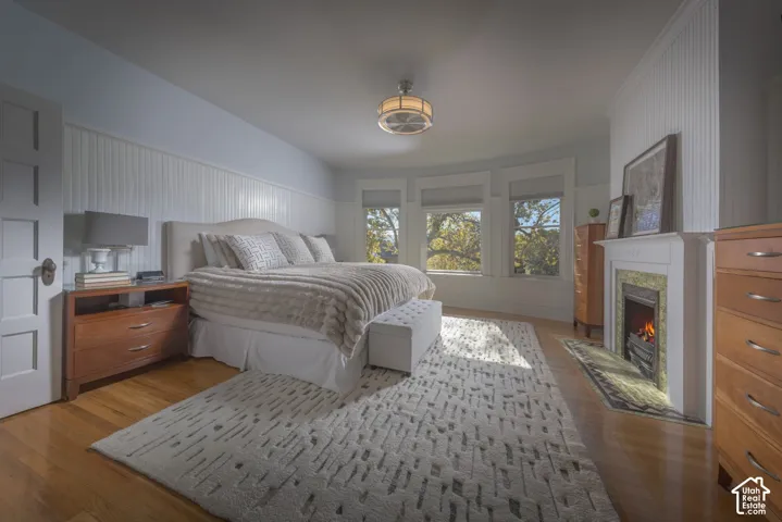 Beadboard wainscoting, wood-finish flooring, fireplace with stone surround, bay window configuration, and drum-style ceiling fixture