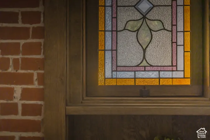 Stained glass window inset featuring decorative geometric and botanical patterns, set within a wood-trimmed frame against exposed brick masonry