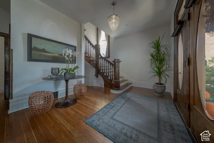 Entryway featuring wood flooring, a stained-wood staircase with ornate railings, a glass pendant light fixture, and a solid wood front door with a decorative oval glass inlay