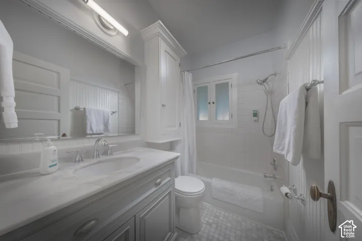 Bathroom featuring a vanity with a light-toned countertop, beadboard wainscoting, a built-in upper storage cabinet, a tiled shower surround, and mosaic tile flooring