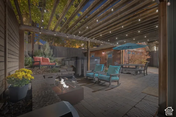 Outdoor living space featuring a wood-beam pergola, brick paver patio, built-in fire feature, and private spa