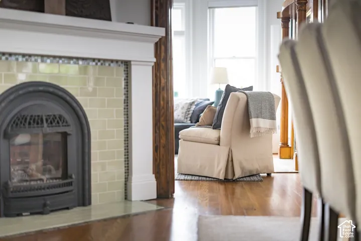 Fireplace featuring a light-toned rectangular tile surround, arched metal insert, and white mantel, complemented by wood-finish flooring and traditional wood trim