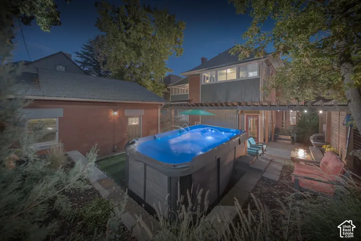 Backyard exterior featuring an above-ground swim spa, a wooden pergola, brick siding, and stone hardscaping