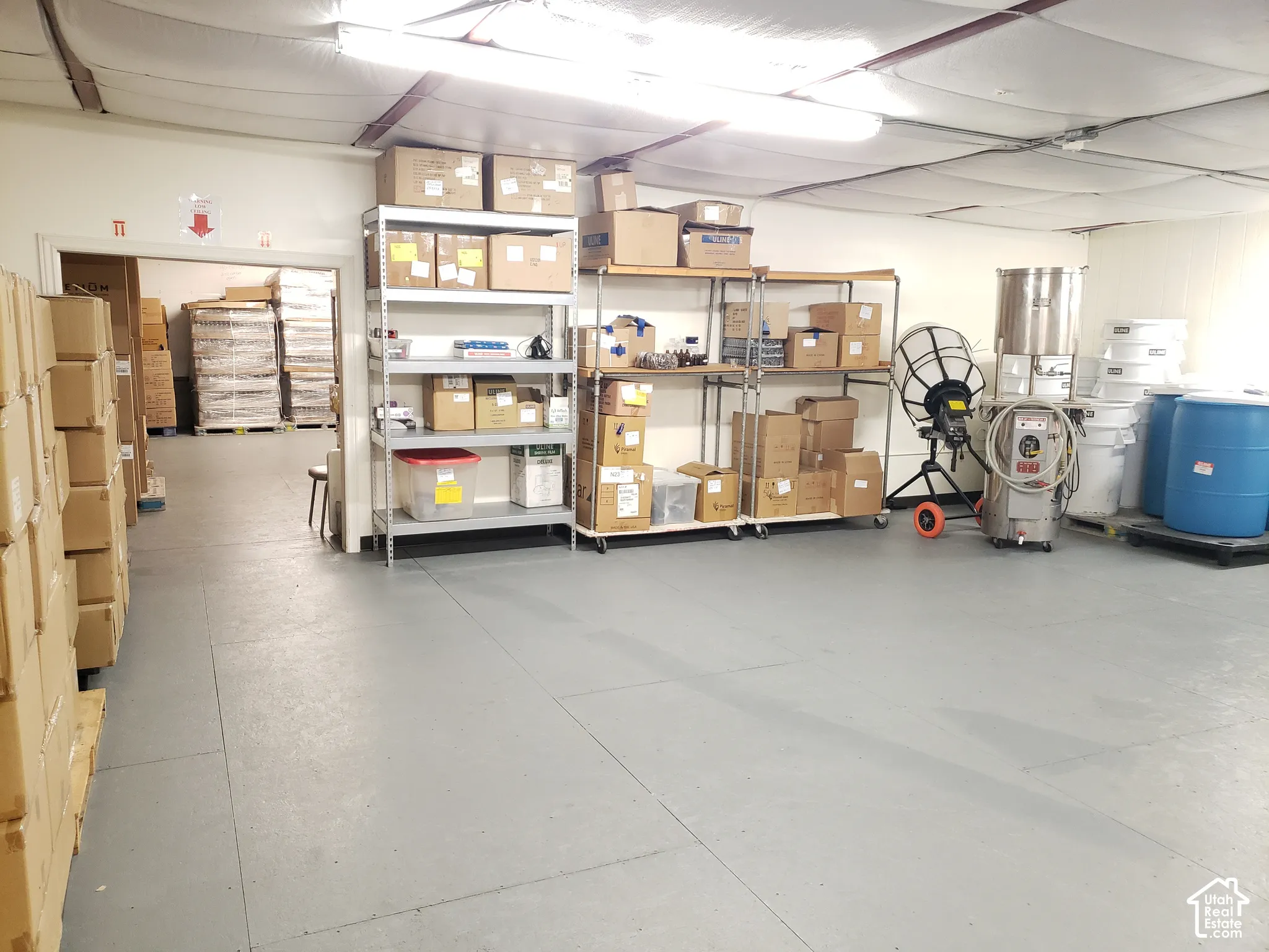 Warehouse space featuring painted concrete flooring, suspended ceiling panels, and linear fluorescent lighting