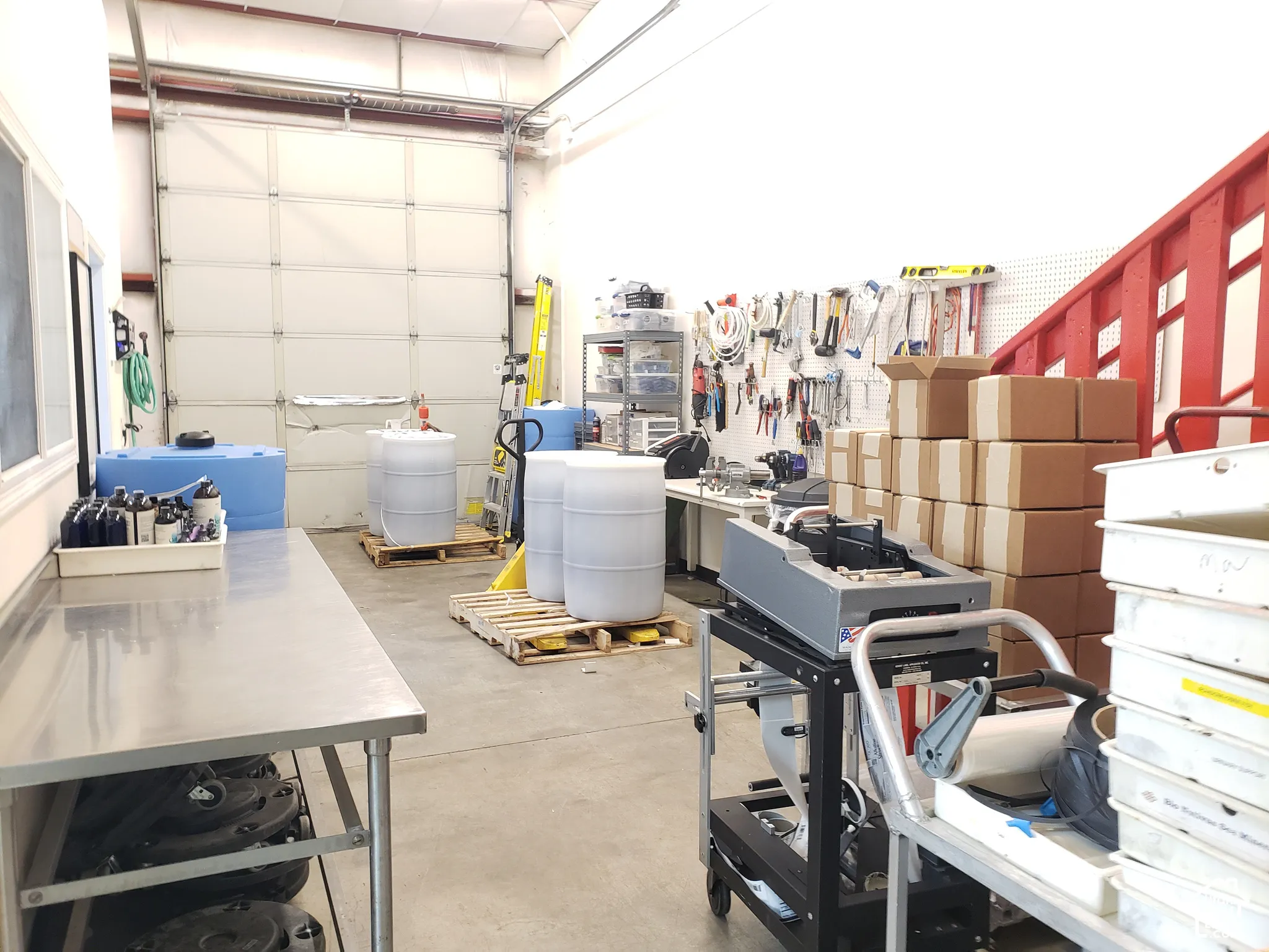 Industrial space featuring high-clearance ceilings, a roll-up garage door, concrete flooring, and a metal staircase