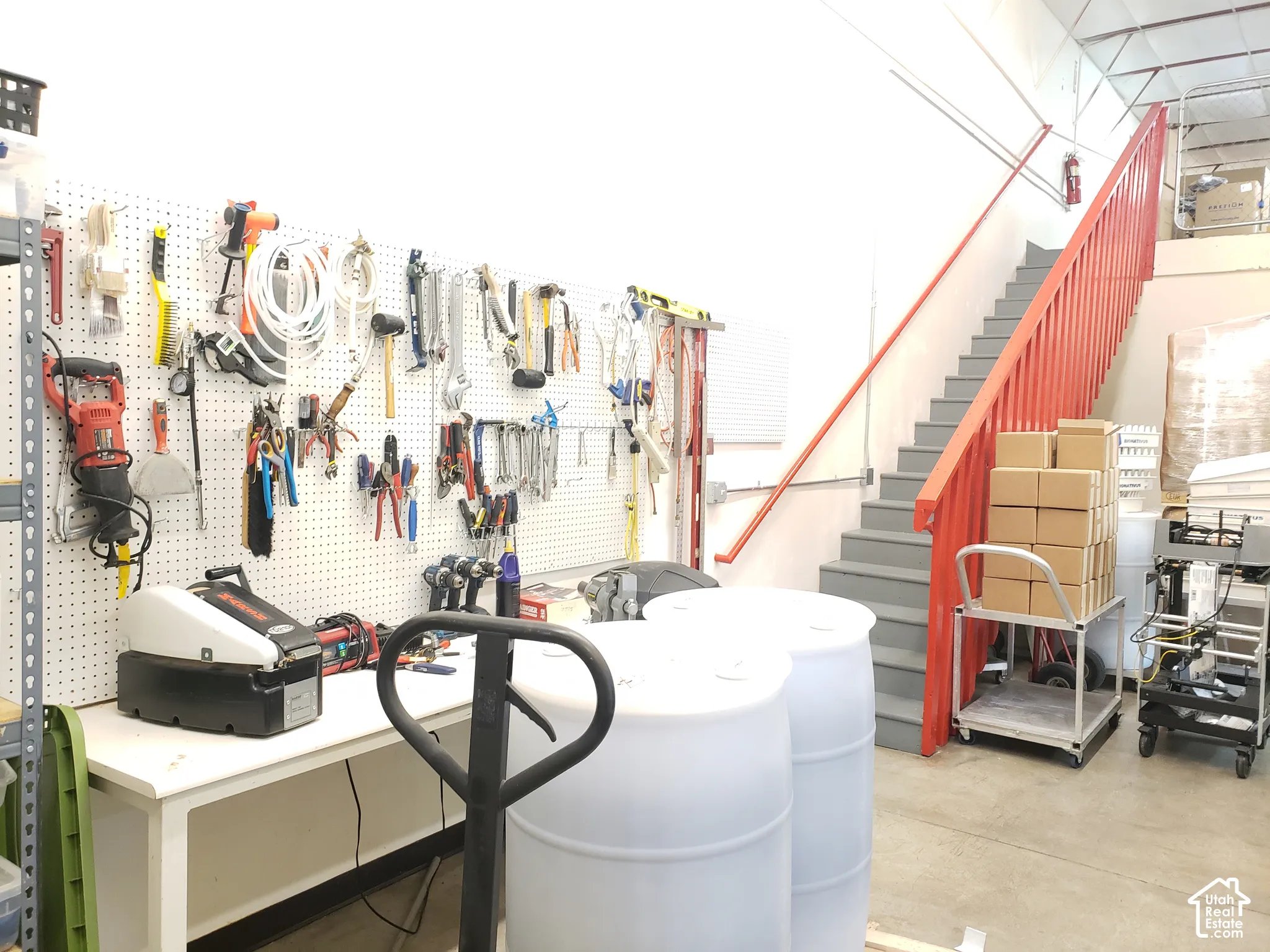 High-ceiling workspace featuring integrated pegboard wall storage, a concrete floor, and a metal staircase with handrails