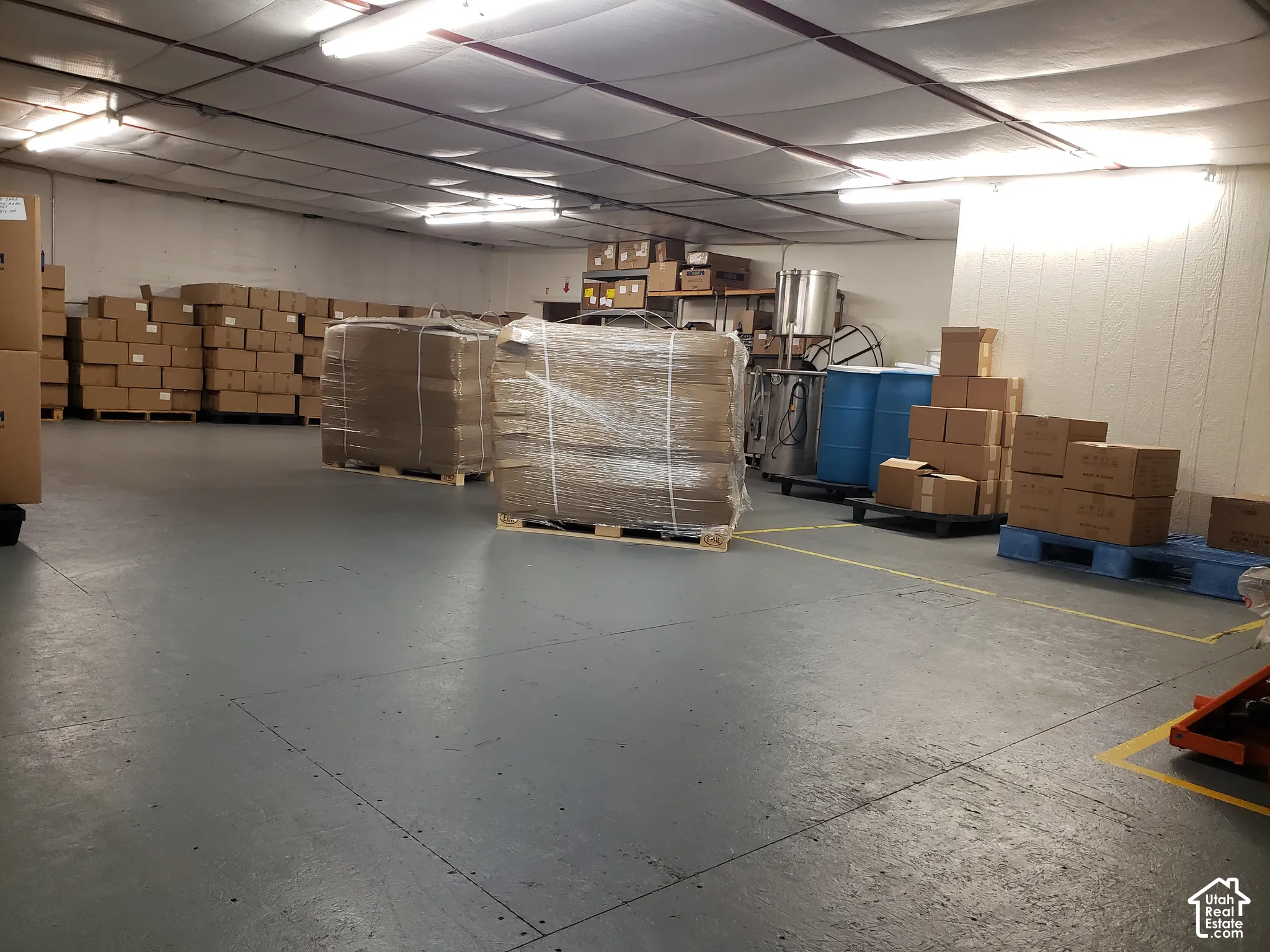 Industrial storage space featuring a sealed concrete floor with painted safety markings, overhead industrial fluorescent lighting, and a suspended ceiling system