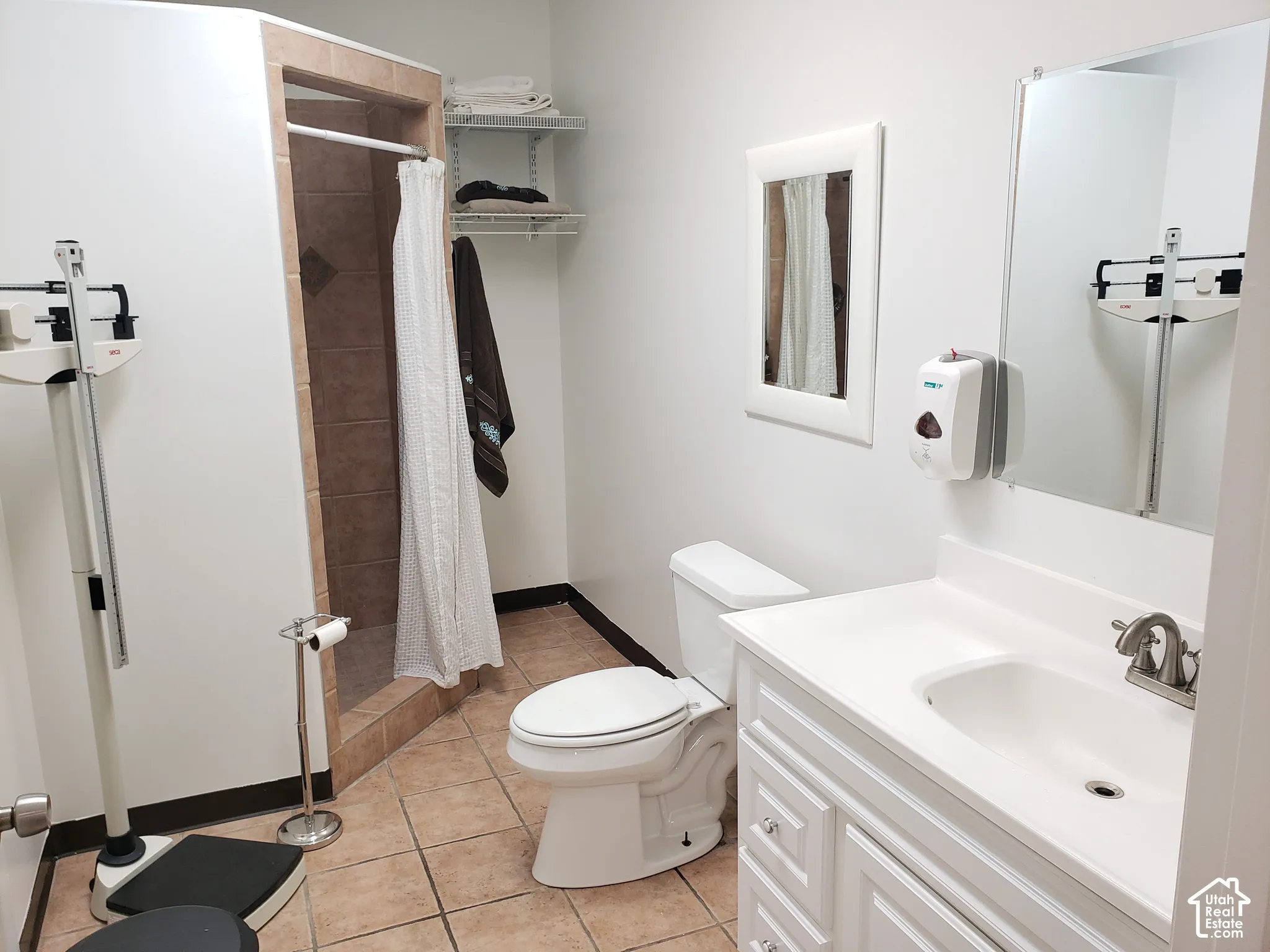 Bathroom featuring a tiled shower enclosure, white vanity cabinet with a integrated basin, wall-mounted mirror, and tile flooring