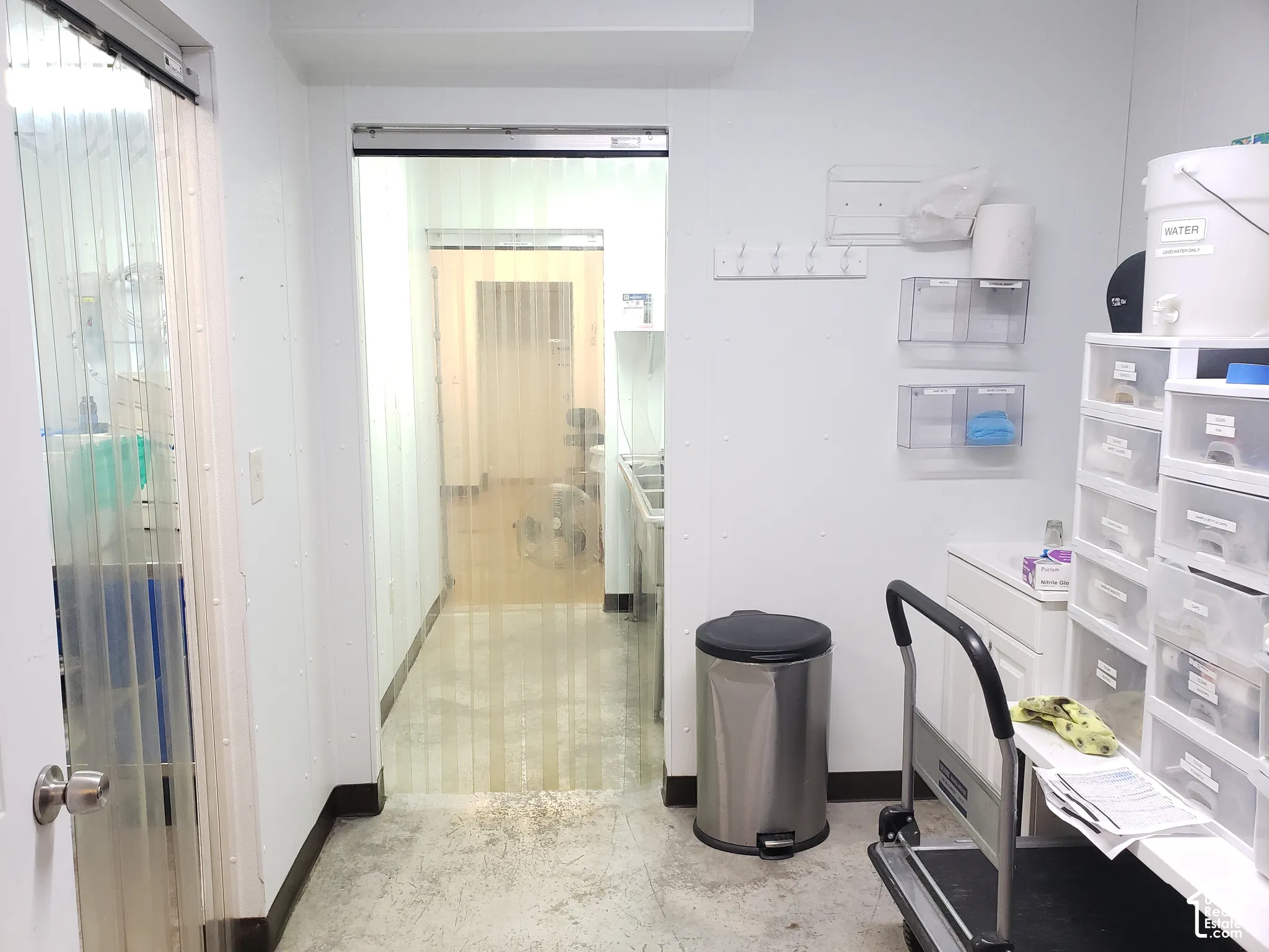 Service area featuring white paneled walls, industrial vinyl strip door curtains, a built-in white vanity, and a wall-mounted coat rack