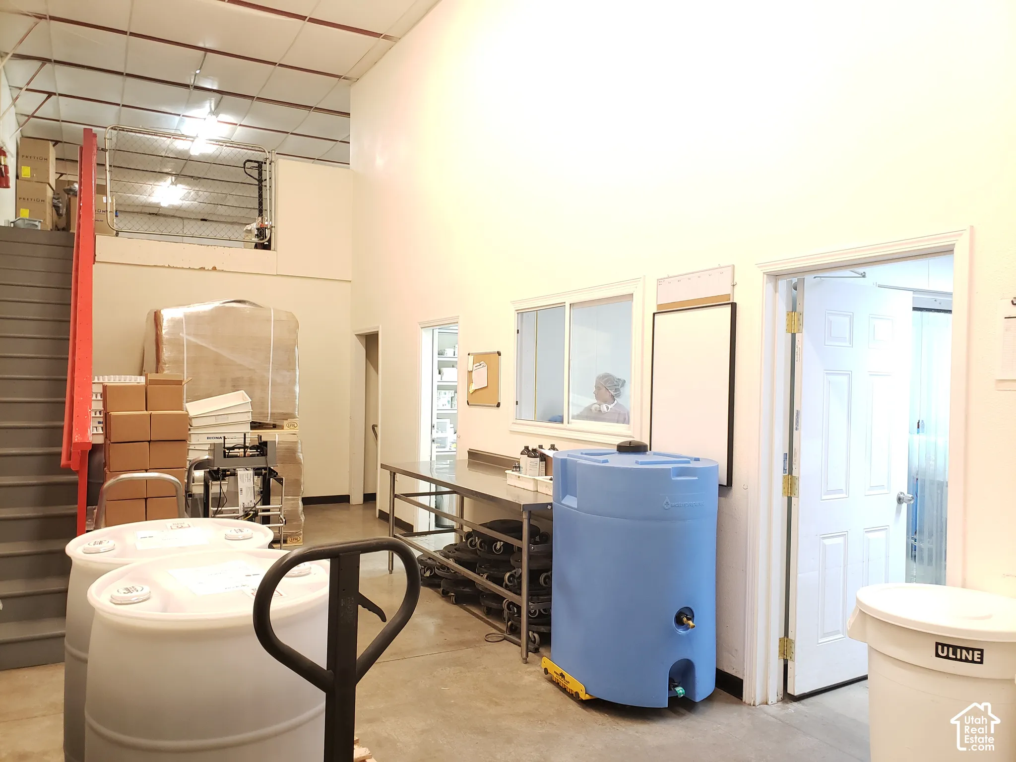 High-ceiling interior space featuring a metal staircase, stainless steel workstation, and internal window partition
