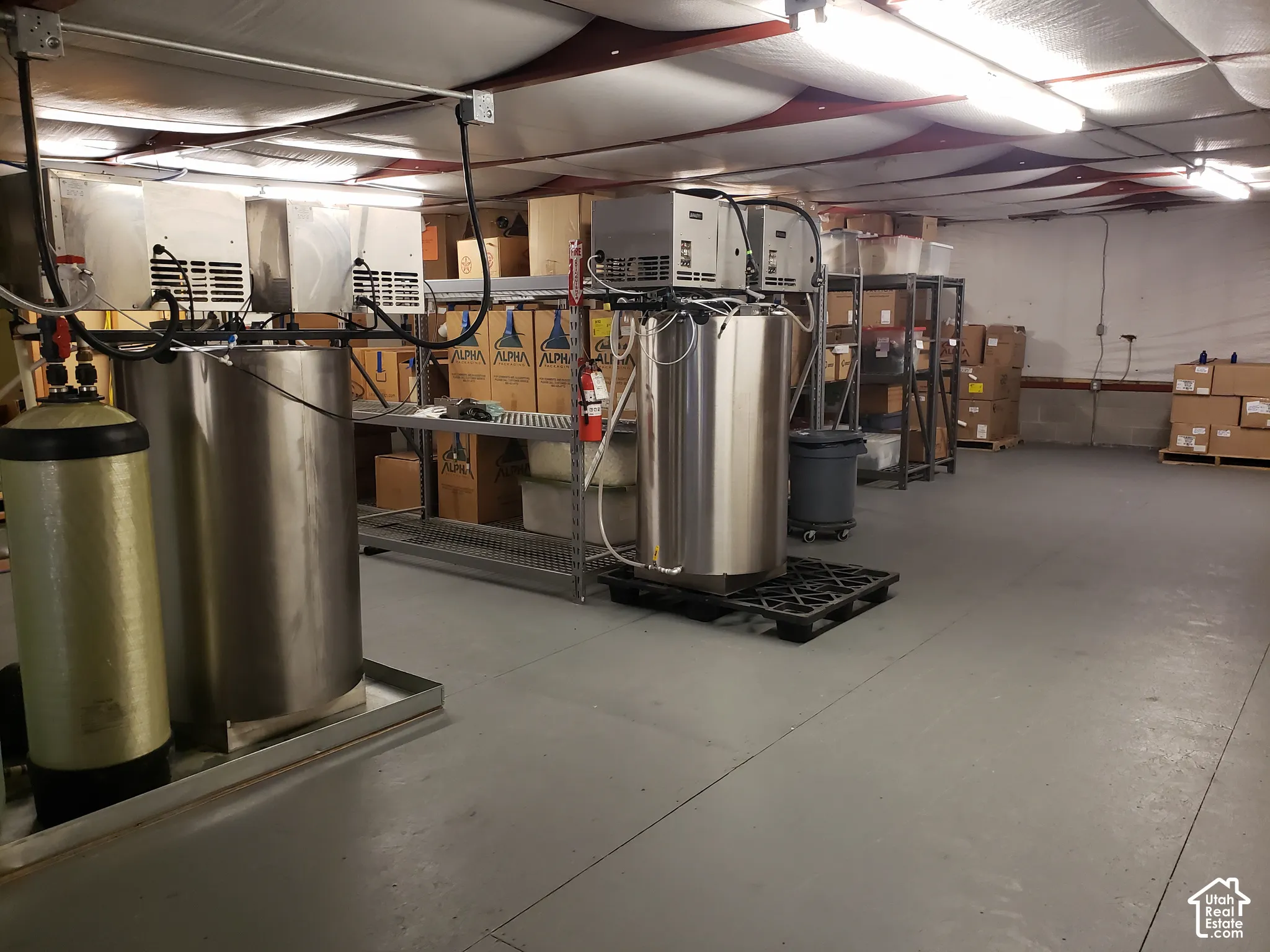 Industrial space featuring reinforced concrete flooring, exposed ceiling lighting, and stainless steel pressurized tank systems with integrated filtration components