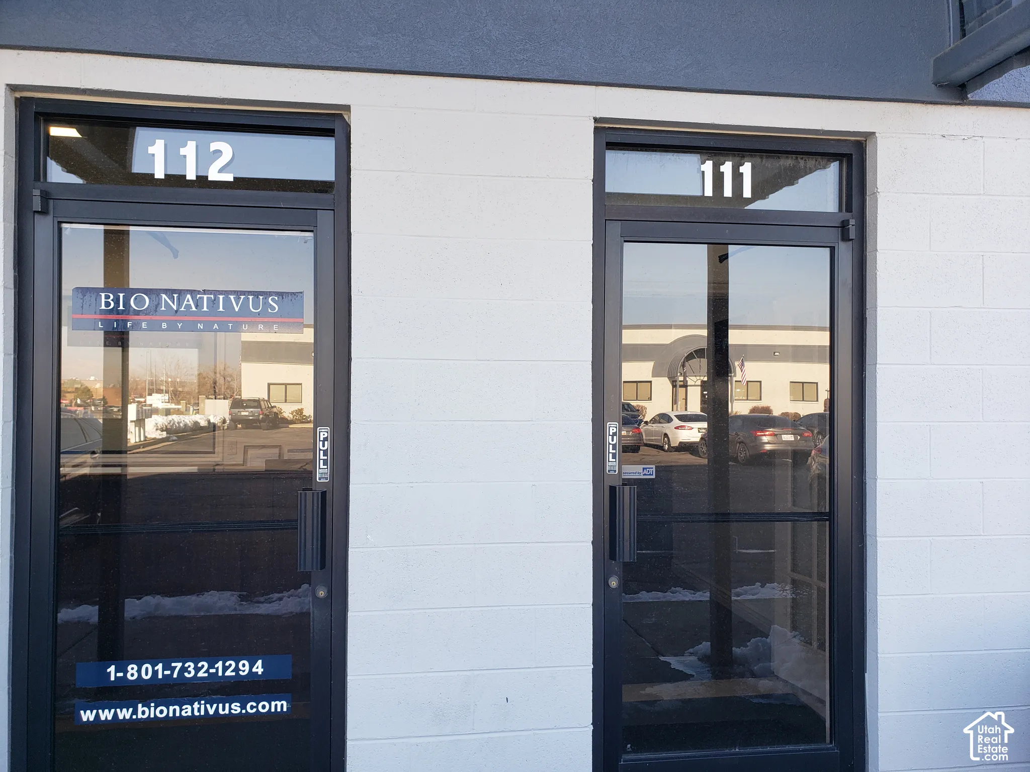 Exterior facade featuring white concrete block walls, dark metal-framed glass doors, and transom windows with numerical signage